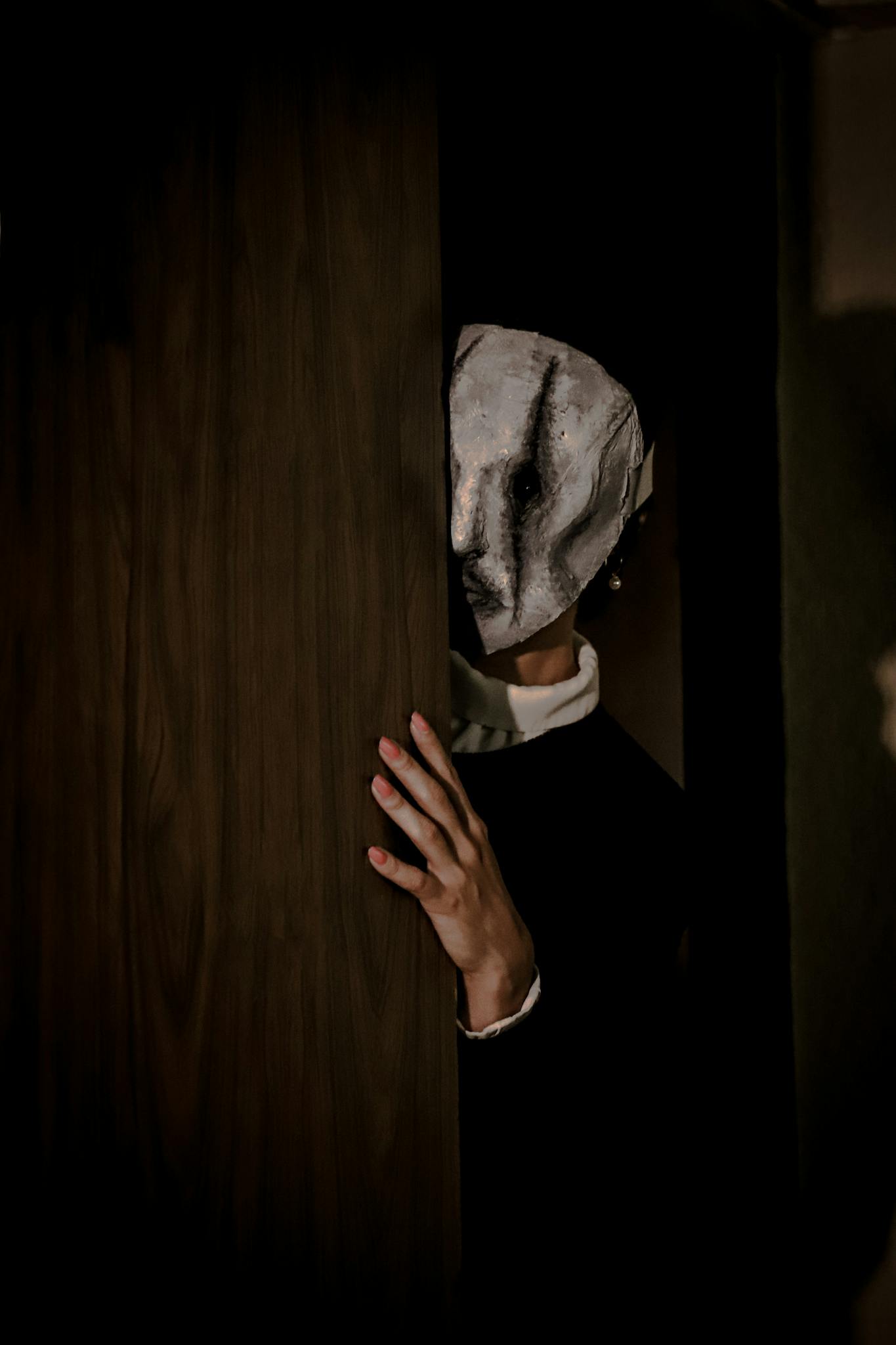 A mysterious figure in a mask peers from behind a door, creating a spooky ambiance.